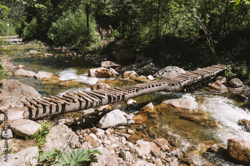 Wooden bridge over a small mountain river in a spring forest. Sunny afternoon.