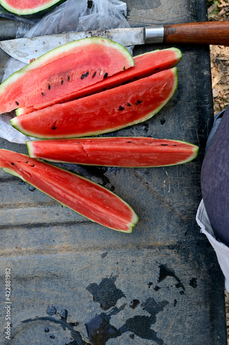 Cut the red ripe watermelon into pieces with a knife on a black background.