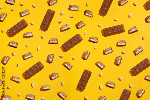 Pieces chocolate bar on a background of peanuts. Modern composition on yellow background
