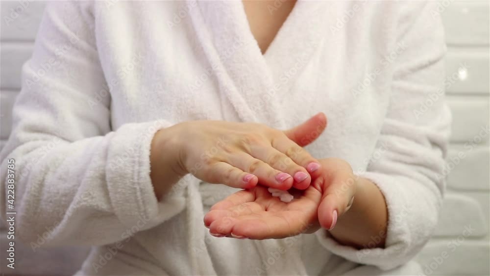 woman in bathrobe squeeze cream from pump bottle on hands skincare cosmetic close up