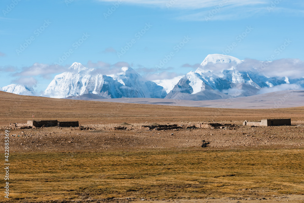 The ruins of a dwelling in the wild grasslands of Tibet and the snow-capped mountains in the distance