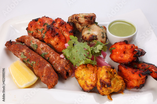 Mixed grill kebab chicken mutton beef prawn fish mint sauce lemon pickled onion coriander on white dish over white background