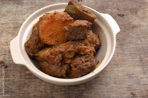 Asian style Beef bhuna dry curry with potato in ceramic bowl over rustic wooden background