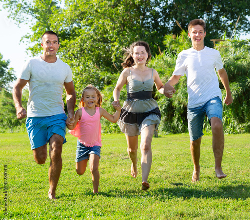 Happy family of four running on grass at summer park. High quality photo