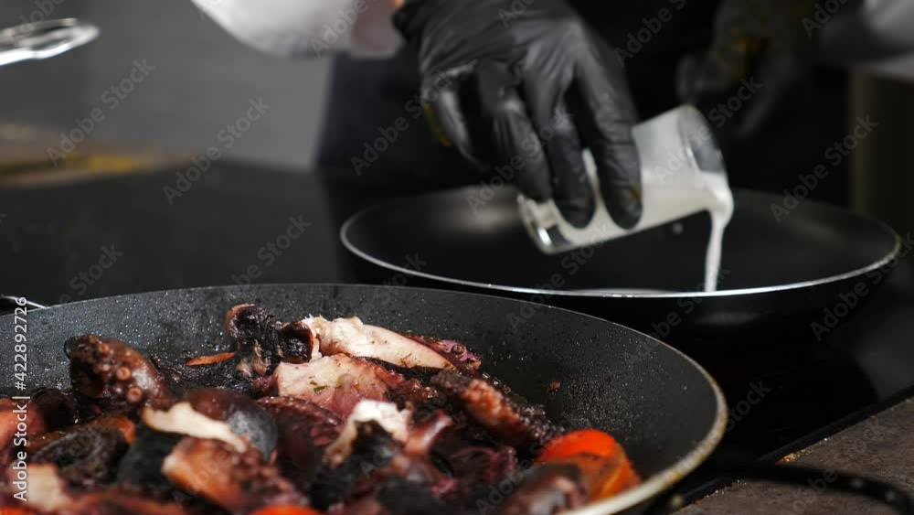 Luxury restaurant. ooking octopus. Pouring milk on frying pan. Cook octopus. Traditional Mediterranean cuisine. Seafood. Chef in black gloves in restaurant kitchen. 4 k video Luxury restaurant. ooking octopus. Pouring milk on frying pan. Cook octopus. Traditional Mediterranean cuisine. Seafood. Chef in black gloves in restaurant kitchen. 4 k video