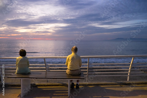An old man stares at the Pacific Ocean while sitting on a bench