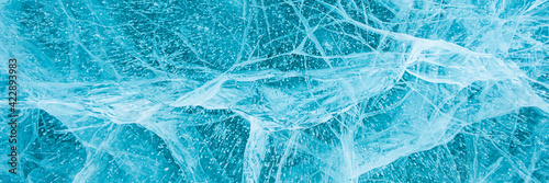 Texture of beautiful blue ice with cracks and air bubbles in the frozen lake. Winter nature background. Lake Baikal, Siberia, Russia. Banner.