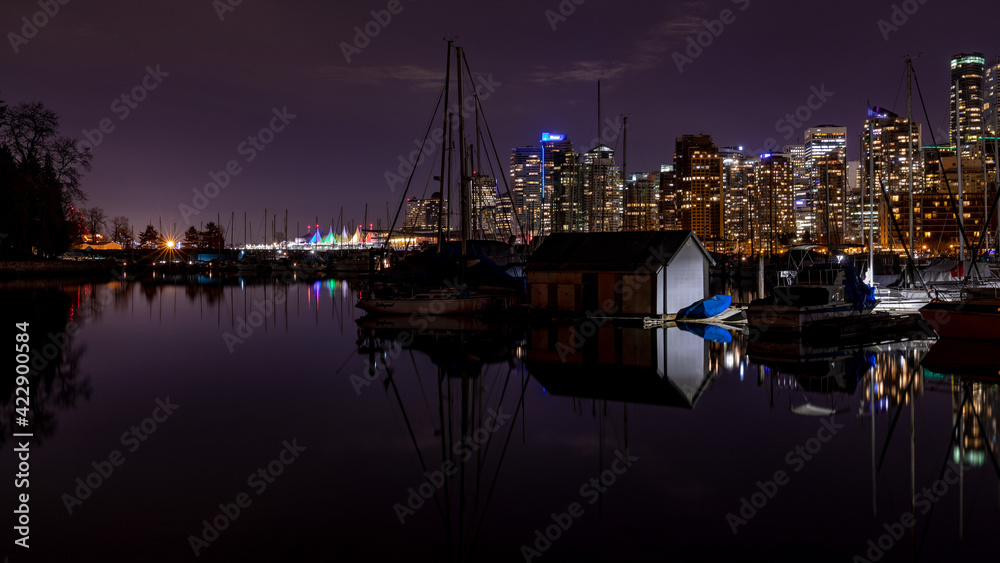 Vancouver, BC \ Canada - 13 March 2019: A night long exposure photo of marina inside Burrard Inlet of Vancouver Harbor with many yachts and boats against colorfully illuminated city skyline