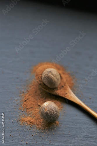 Nutmeg spice.Whole and ground nutmeg in a wooden spoon  on a black schiffer background.Spices and herbs.Food ingredient.Spices for meat and baking.Nutmeg powder