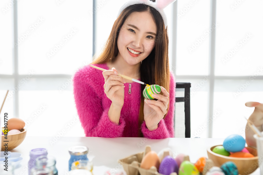 Easter holiday concept, Happy Asian Young woman wearing bunny ears hand painted eggs for Easter with colorful Easter eggs In the white room background Easter holiday concept, Happy Asian Young woman wearing bunny ears hand painted eggs for Easter with colorful Easter eggs In the white room background