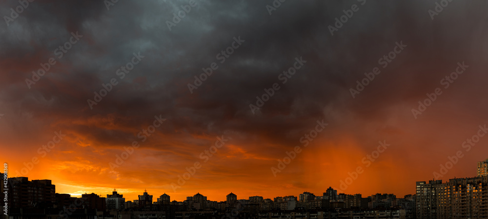 Wide angle shot of dramatic stormy sunset sky with clouds over city skyline background.