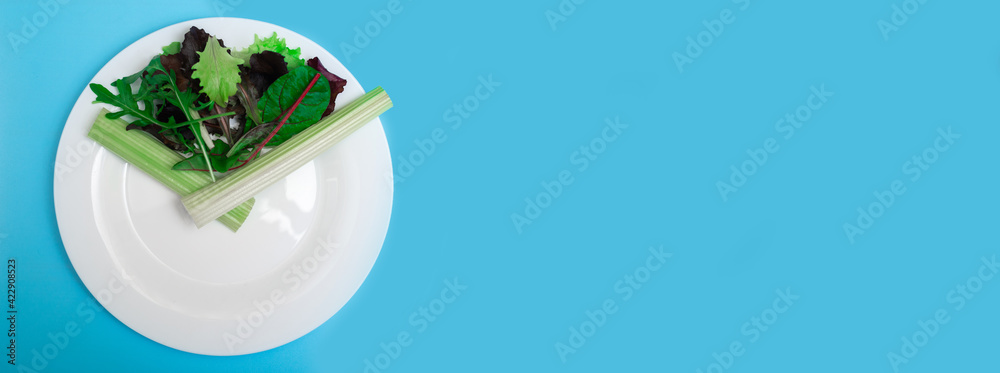 Intermittent fasting, diet concept. Figurative image of meal time. Fresh vegetables on a white plate as a clock face on a light blue background. Banner. Place for your text. Intermittent fasting, diet concept. Figurative image of meal time. Fresh vegetables on a white plate as a clock face on a light blue background. Banner. Place for your text.