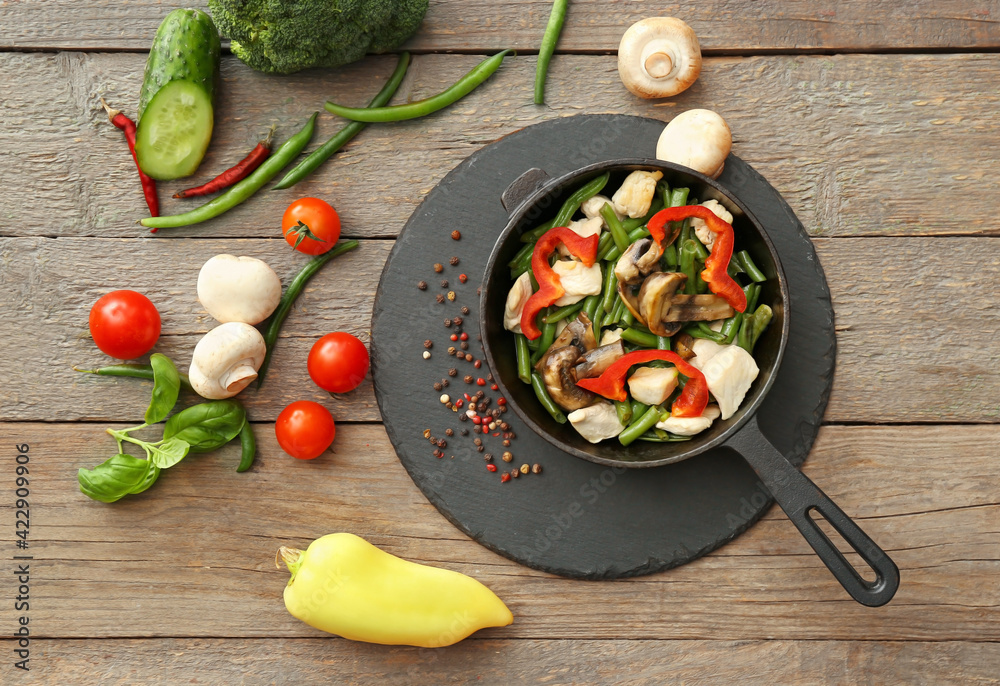 Frying pan with tasty vegetables and chicken on wooden background Frying pan with tasty vegetables and chicken on wooden background