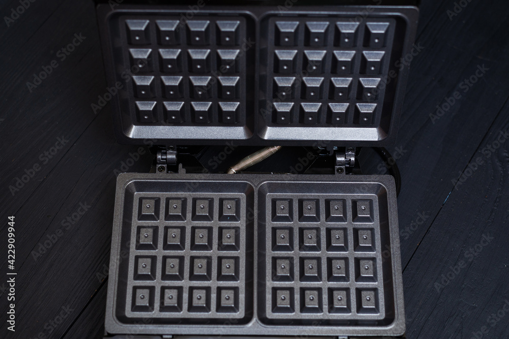 Electric waffle iron on a black wooden background. Device for making Belgian waffles. Electric waffle iron on a black wooden background. Device for making Belgian waffles.