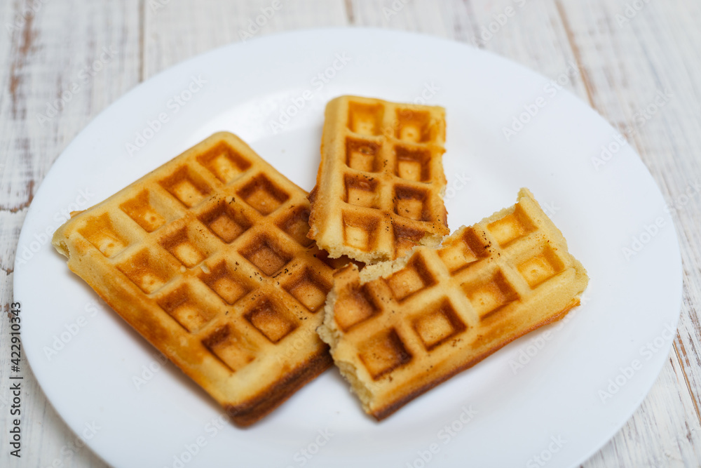 Freshly cooked Belgian waffles on a white plate on a light wooden background. Freshly cooked Belgian waffles on a white plate on a light wooden background.