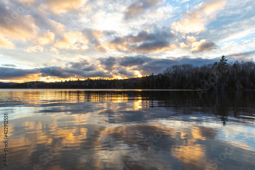 Fototapeta Naklejka Na Ścianę i Meble -  Fin d'un coucher de soleil avec lumière jaune sur un lac avec surface miroitant les nuages