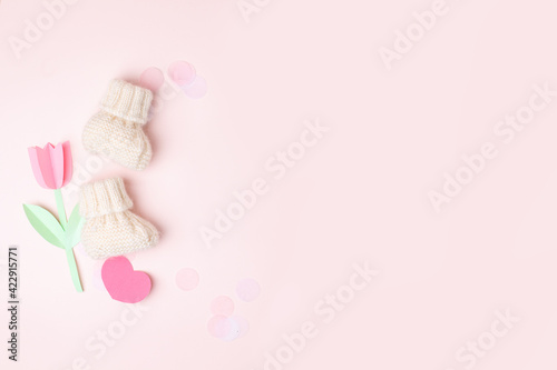 Pair of small white baby socks with and paper decorative flowers on pink background with copy space for your warm message, baby shower, first newborn party background, copy space