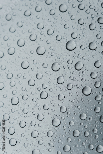 Close-up of water droplets and drops on a gray surface. Texture and structure after rain. Ecology. Vertical photography. Drops of different sizes.