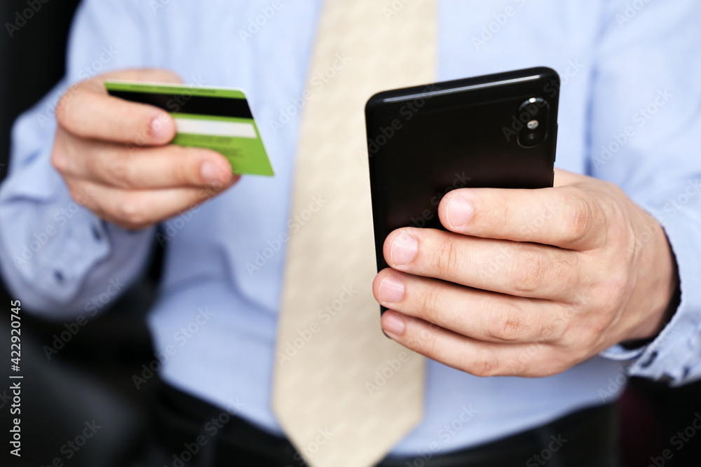 Man in office clothes holding credit bank card and smartphone in hands. Concept of online shopping and payment, financial transaction