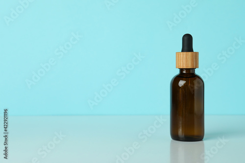 Dropper bottle with oil against blue background, space for text