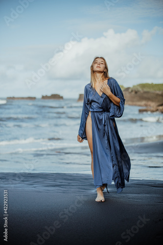 Photoshoot of a blonde girl in a blue dress on the Bali beach with black sand