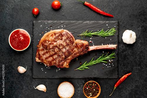 Grilled tomahawk beef steak with spices on stone background