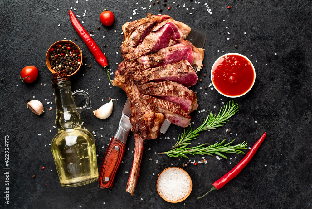 Tomahawk beef steak with spices on a knife on a stone background