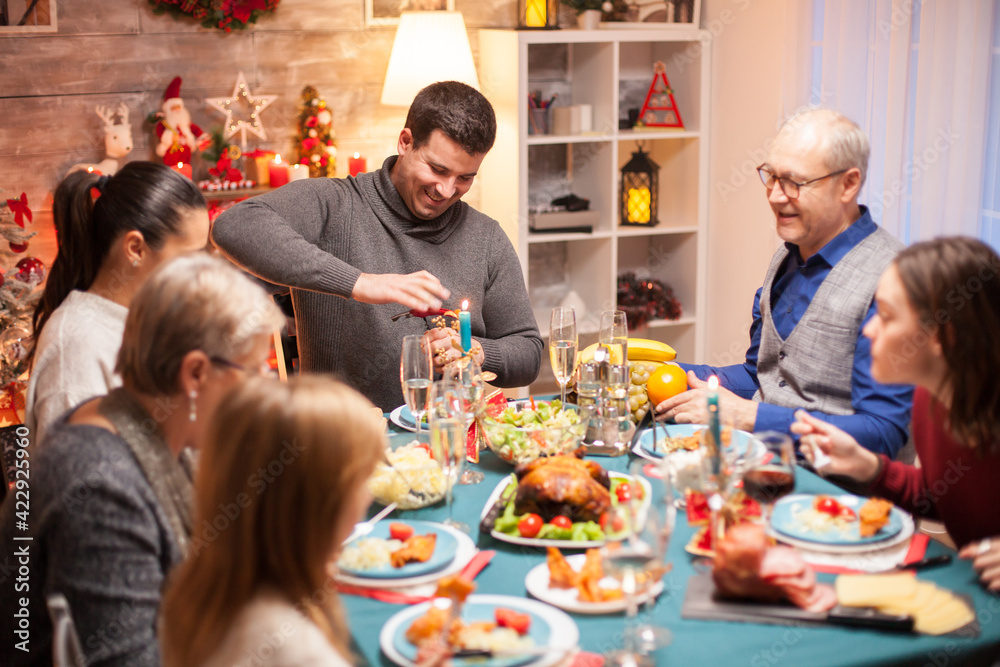 Cheerful young man opening a bottle of wine at christmas family dinner.