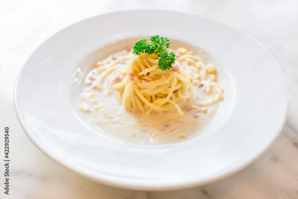 Spaghetti in white cream sauce mixed with ham and corn and served on a white plate in Italian food restaurant. Spaghetti in white cream sauce mixed with ham and corn and served on a white plate in Italian food restaurant.