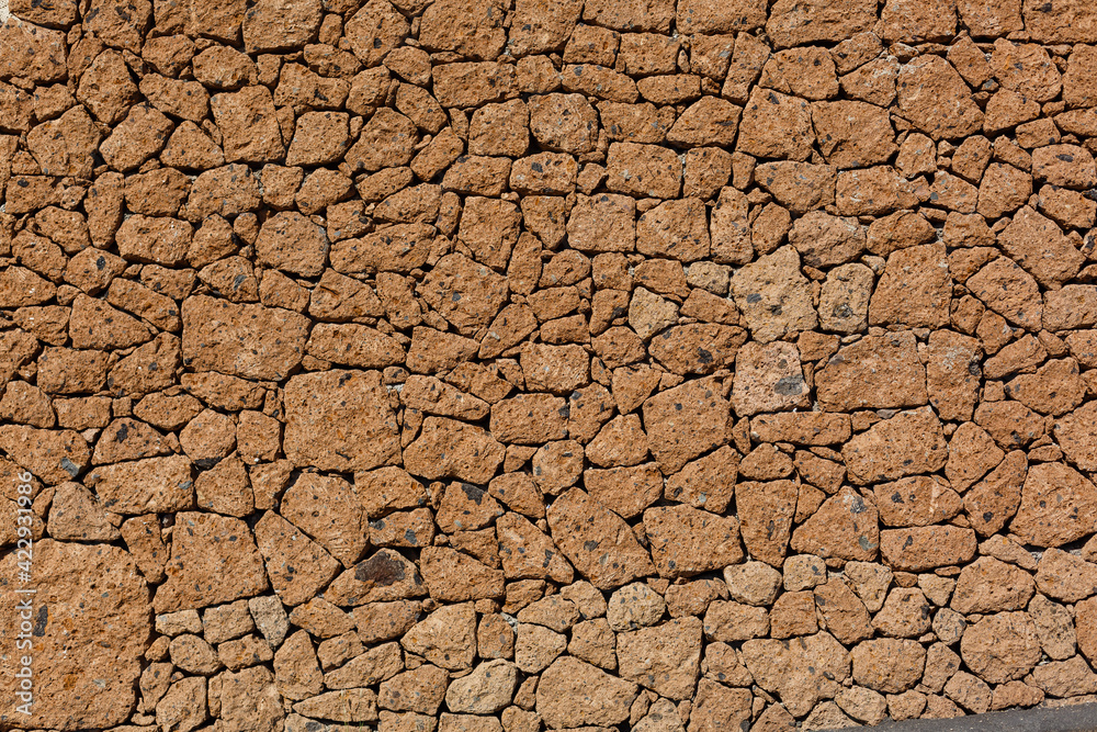 Stone fence texture - building feature. Texture of concrete fence with relief and texture like an orange stone wall Stone fence texture - building feature. Texture of concrete fence with relief and texture like an orange stone wall