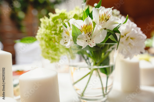 Beautiful flowers in vase, close up. Festive table decorated with white and green composition, candles in the banquet hall. Newlyweds table in banquet area for wedding. Film noise