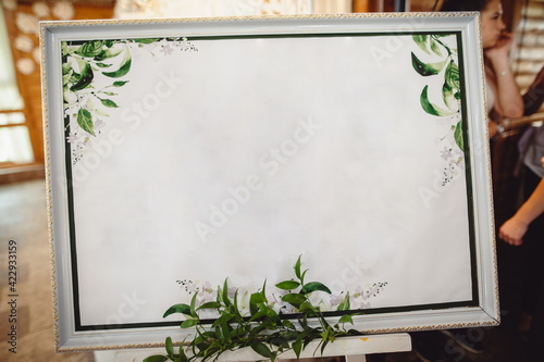 List, plan, of the seating area of guests at the tables at restaurant. Tables wedding guests on the easel on reception. The frame is decorated. Blank sheet of paper in the frame. Film noise 