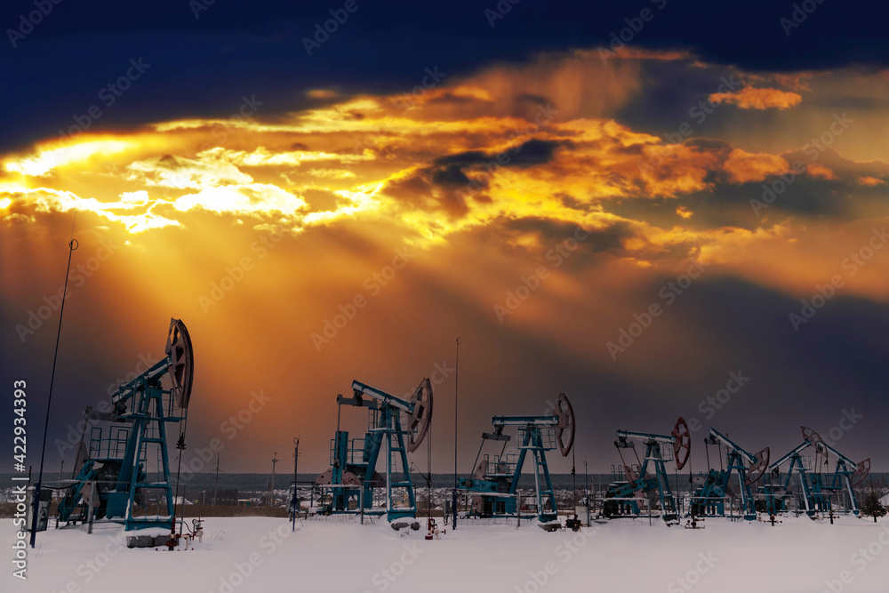 Oil pumpjack winter working. At the orange sunset dawn of the sky with clouds. Oil rig energy industrial machine for petroleum in the sunset background for design. Nodding donkey
