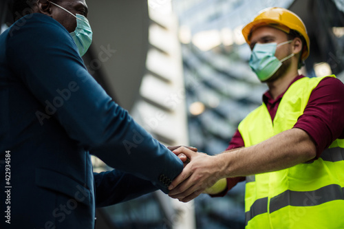 Two businessmen handshaking. Business men wearing protective mask. © liderina