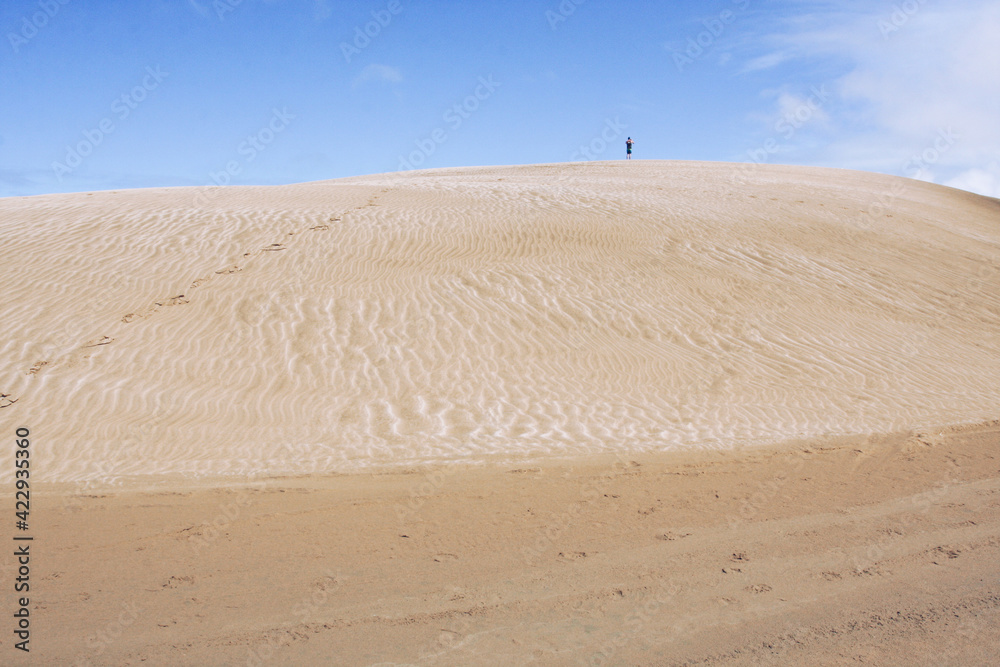 Sand dunes hill with a man silhouette on the blue sky background