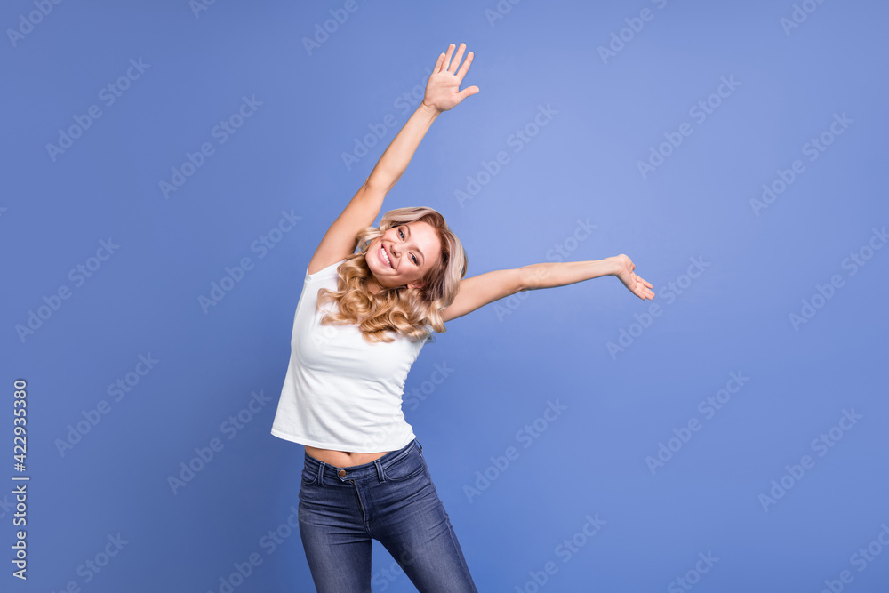 Portrait of charming cheerful wavy-haired girl dancing having fun stretching isolated over blue color background Portrait of charming cheerful wavy-haired girl dancing having fun stretching isolated over blue color background
