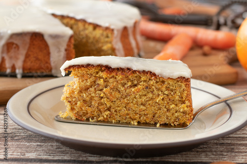 Piece of fresh baked carrot cake with lemon glaze on a plate with cake server