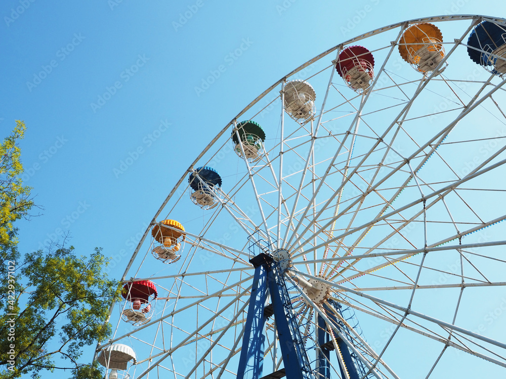 Ferris wheel with multi-colored booths against a clear blue sky. Bottom view. Soviet era amusement ride Ferris wheel with multi-colored booths against a clear blue sky. Bottom view. Soviet era amusement ride