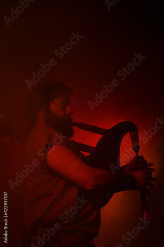 Bagpipe player in dramatic red light. Celtic music concert photo. Man with beard plays a big hornpipe.