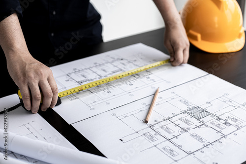 An engineer is using a tape measure to measure the plans of the house that he designs, the drafts the house drawings to build the correct standard. Engineer concept.