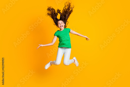 Full size photo of happy excited funky funny little girl jumping with flying hair isolated on yellow color background