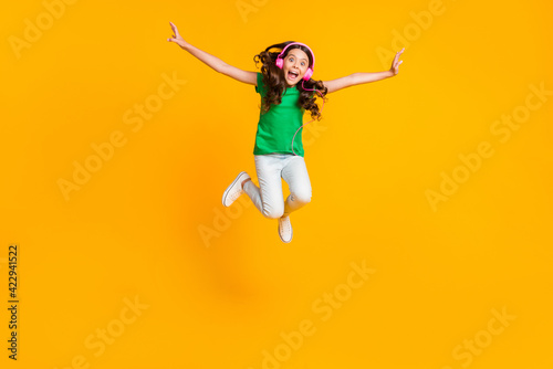 Full size photo of happy excited crazy smiling funky girl jumping listen music in earphones isolated on yellow color background