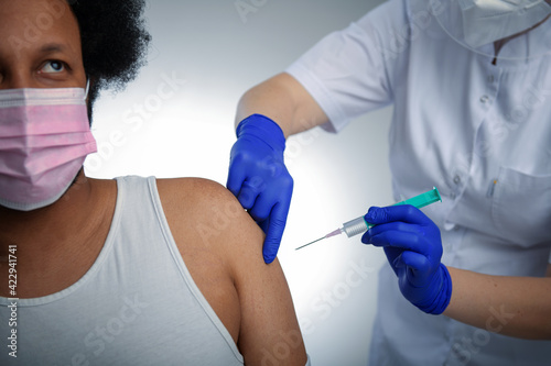 African American male patient getting immunized against covid-19, receiving antiviral vaccine injection. Studio photo, concept, white blue background
