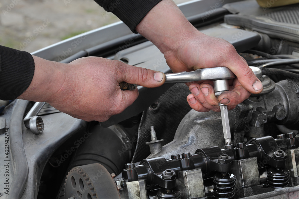 Car mechanic fixing modern diesel engine, closeup of hand with ratchet wrench, removing injectors from cylinder head with camshaft and rocker arms