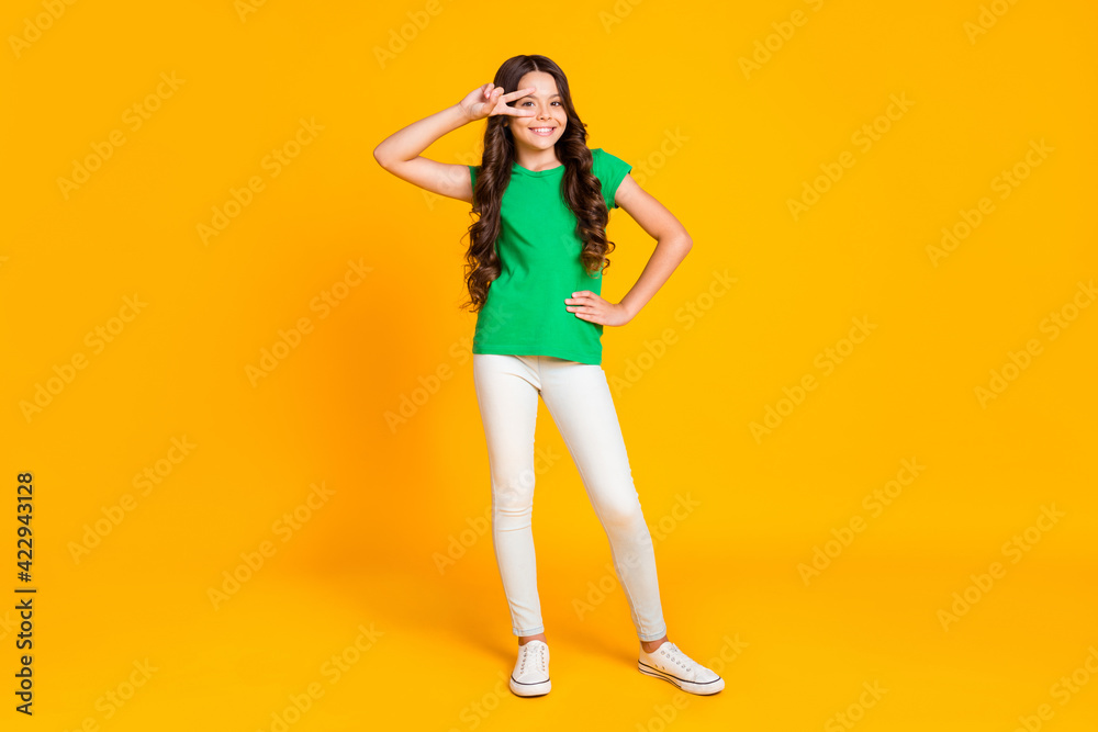 Full size photo of young cheerful good mood lovely cool little girl showing v-sign on eye isolated on yellow color background