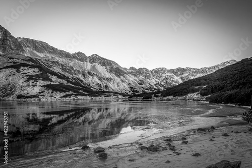 Black and white view of Dolina Pięciu Stawów Polskich, Tatra Mountains, Poland. A valley with a lake which is starting to freeze. Selective focus on the rocks, blurred background.