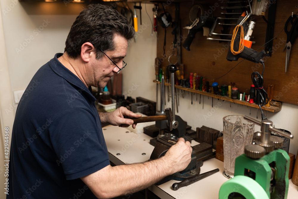 jeweler goldsmith picks a piece of square with a hammer on an anvil jeweler goldsmith picks a piece of square with a hammer on an anvil