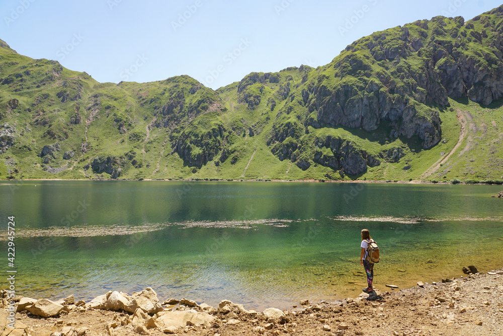 A girl with a backpack is looking to a lake in the mountain