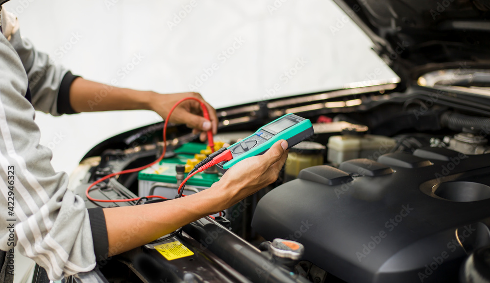 A technician is checking the car battery for availability.; A technician is checking the car battery for availability.;