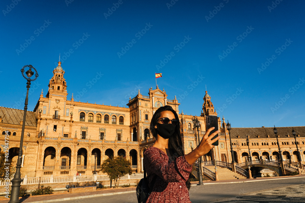 Fototapeta premium Young and pretty woman making selfie with facemask in Spain Square, Seville.